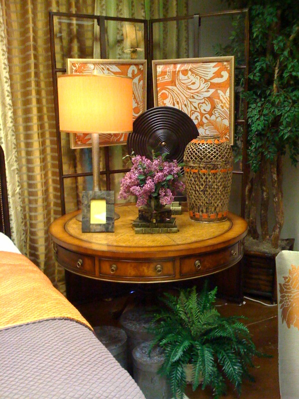 Lamp, floral, basket weave vase, & wood charger on a stand are all in scale with the large round bedside table